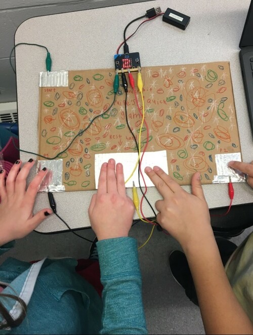 Student work area with 2 sets of hands working on a Micro:Bit with Gator Clips.